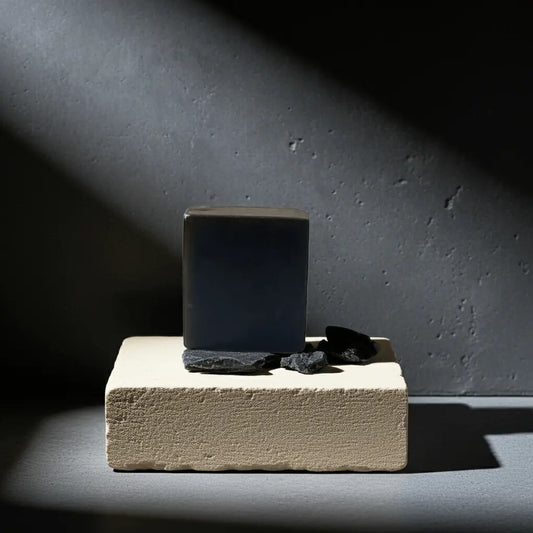 Urban Tree Charcoal Activated Soap bar on beige stone block with natural charcoal pieces and spotlight effect