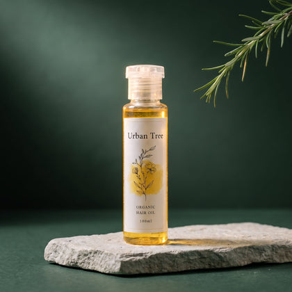 Urban Tree Organic Hair Oil 100ml bottle of golden herbal oil on a stone slab against a deep green background