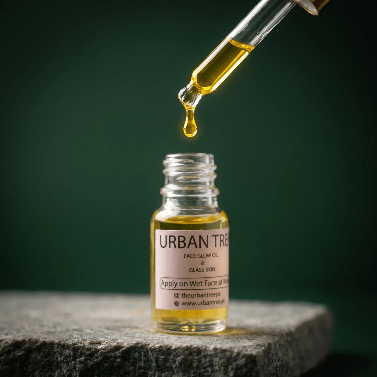Close-up of Urban Tree Glass Skin Elixir golden face oil dropping from a glass pipette into the bottle