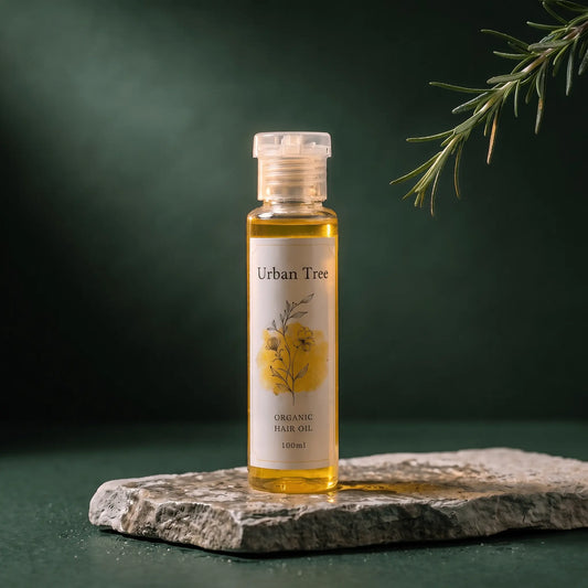 Urban Tree Organic Hair Oil with Rosemary 100ml bottle on a stone slab with a rosemary sprig, deep green backdrop